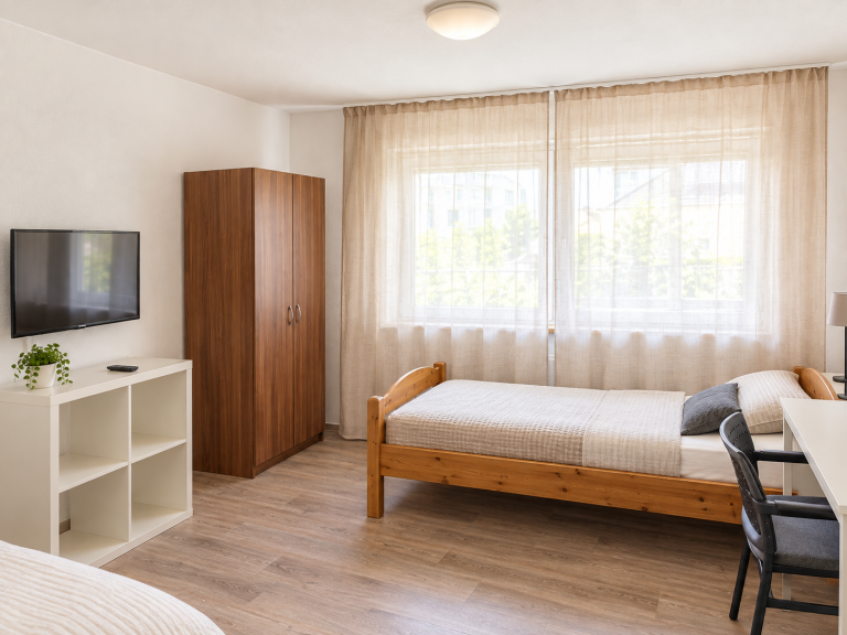 Helles Zimmer mit zwei Einzelbetten, Tisch, Stühlen und Fenster mit Vorhängen. Monteurzimmer Mannheim